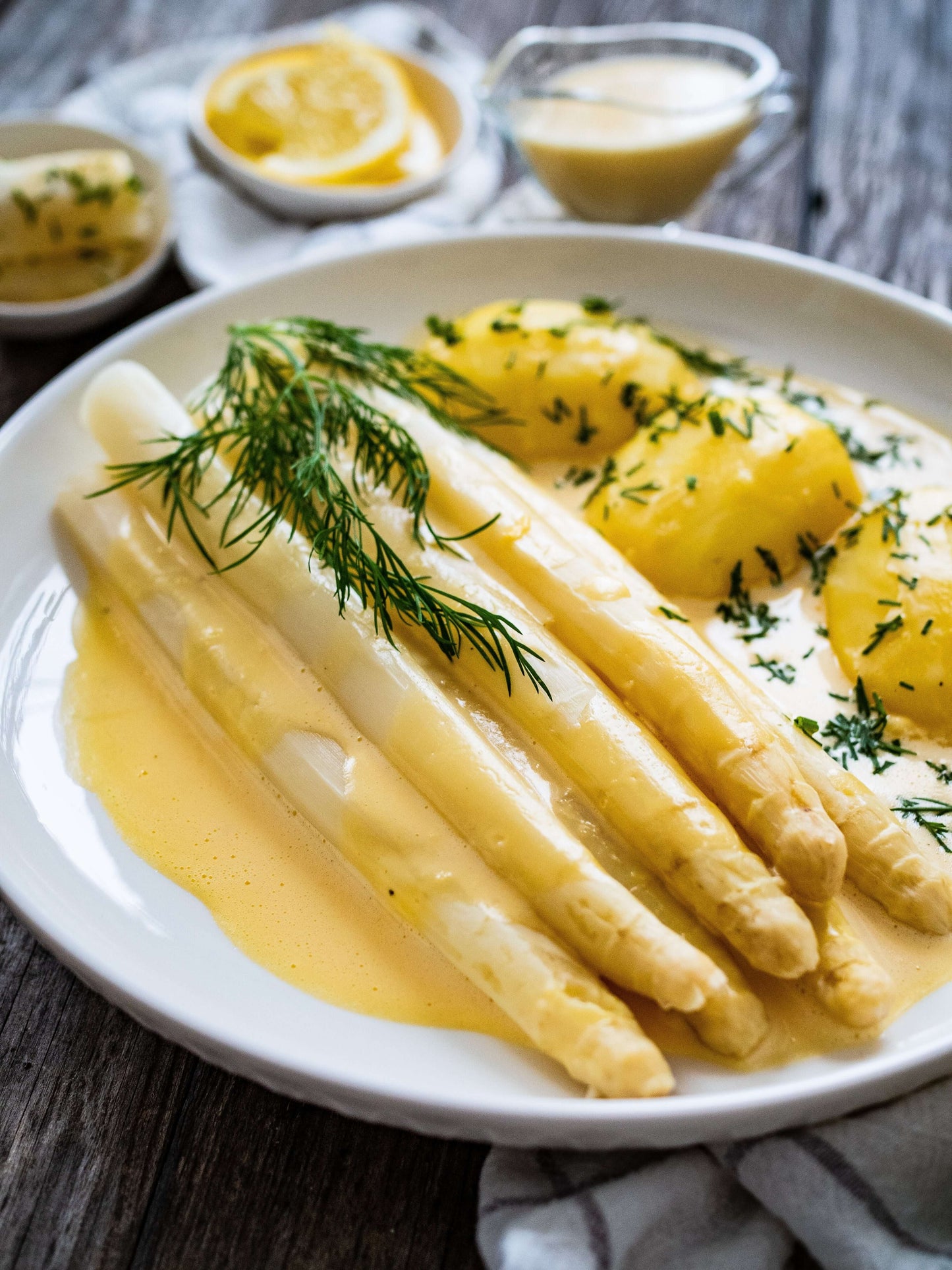 Plate of French Jumbo White Asparagus served with sauce and potatoes, garnished with fresh herbs.