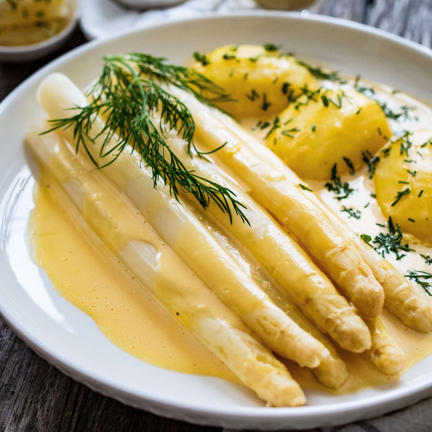 Plate of French Jumbo White Asparagus served with sauce and potatoes, garnished with fresh herbs.