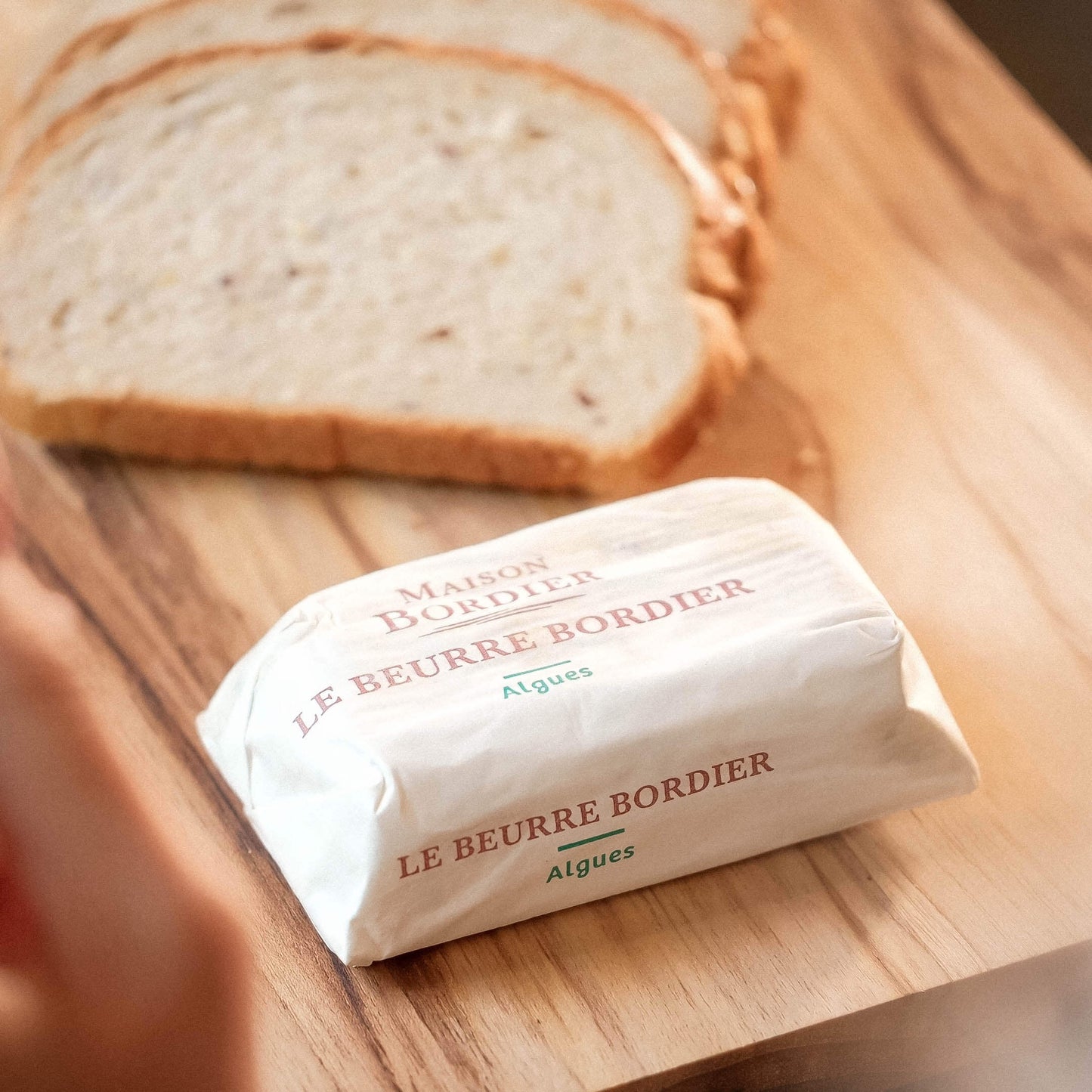 Le Beurre Bordier Seaweed Butter wrapped with slices of bread on a wooden cutting board.