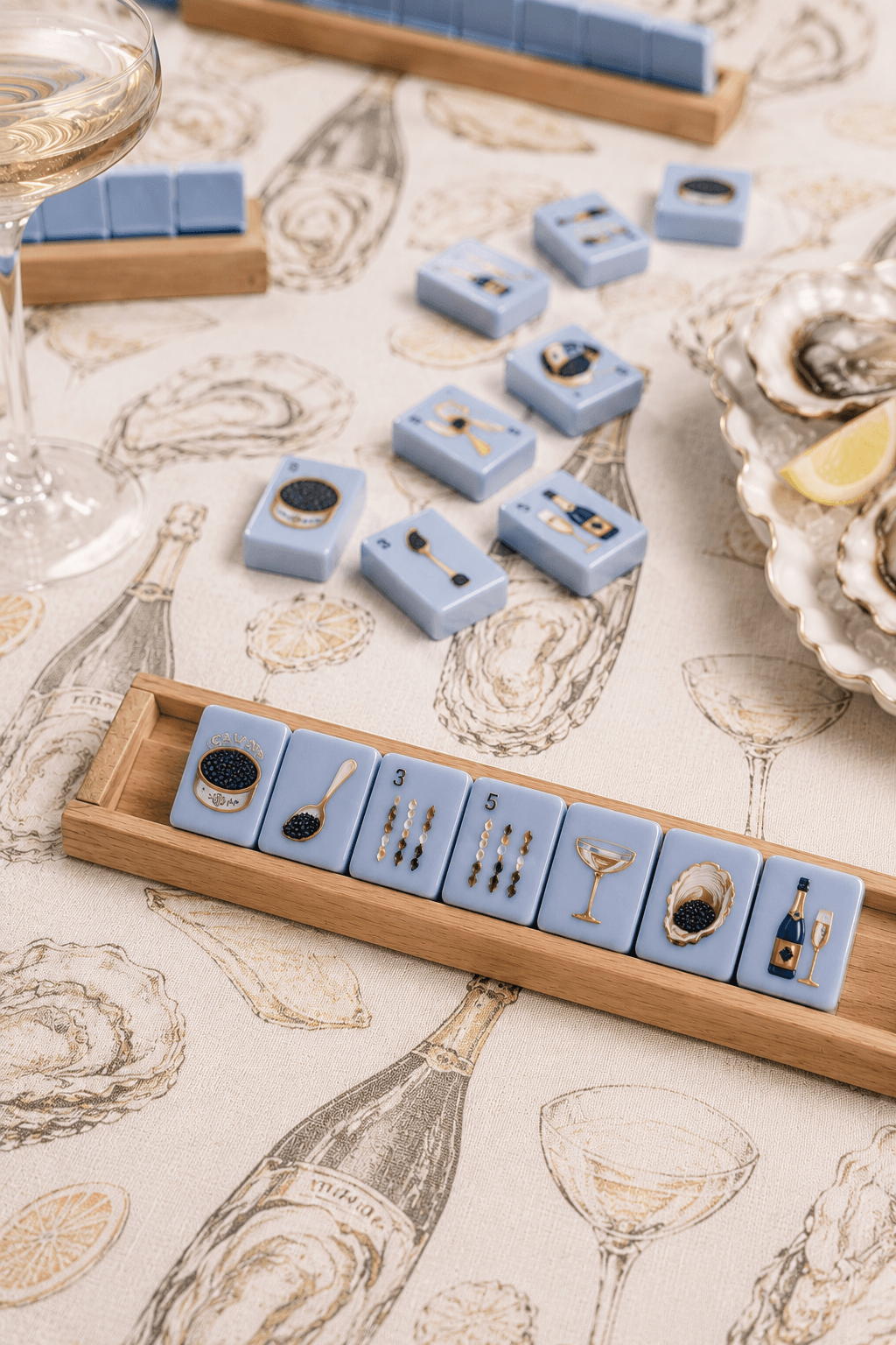 A stylish table setting with blue Mahjong tiles, champagne glasses, and an oyster plate, perfect for a chic gathering.