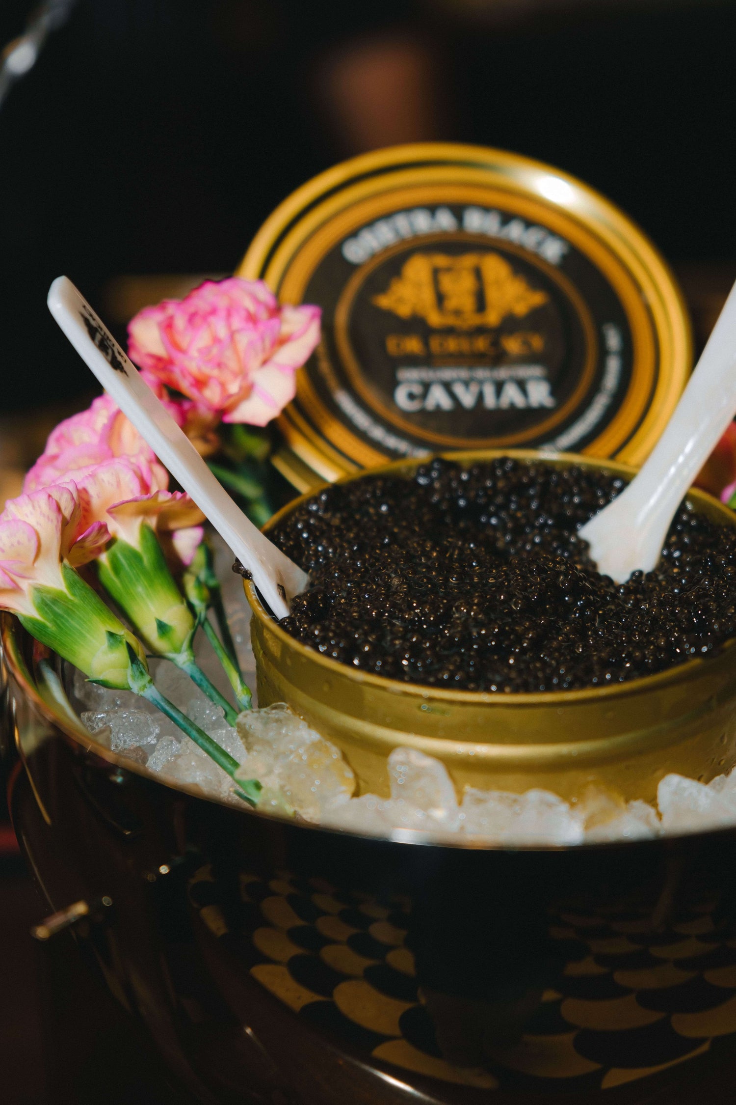 Gourmet caviar in a golden tin surrounded by ice and pink flowers, ready for an elegant dining experience.