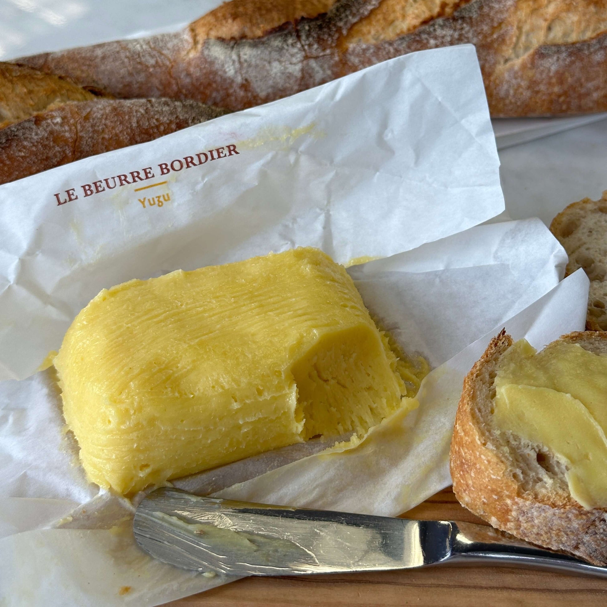 Butter with a knife and bread on a white paper with 'Le Beurre Bordier' branding.