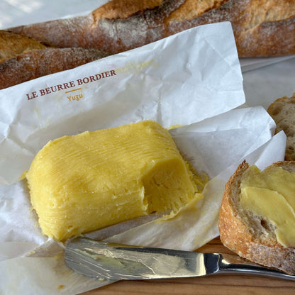 Butter with a knife and bread on a white paper with 'Le Beurre Bordier' branding.