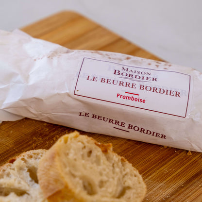 Le Beurre Bordier Raspberry Butter packaging next to sliced bread on a wooden cutting board.
