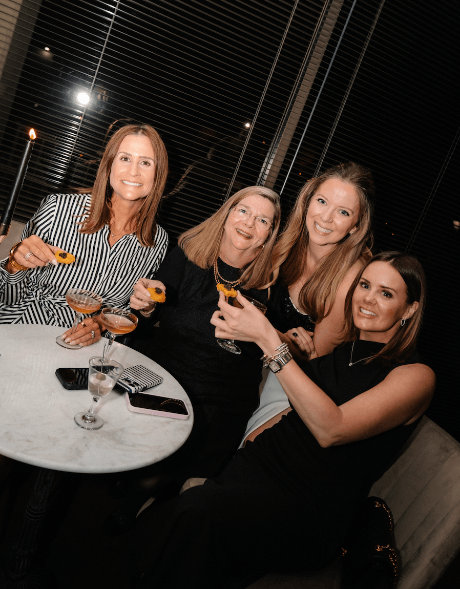 Four women enjoying cocktails and appetizers at a stylish evening gathering.