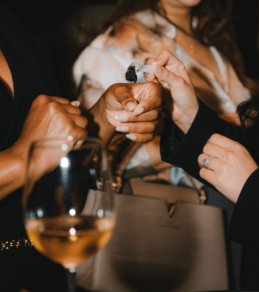 Hands exchanging a luxurious treat at a social gathering, with a glass of wine in the foreground.